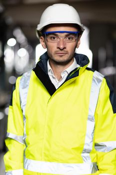 Caucasian Industrial Specialist Standing in a Metal Construction Manufacture. Professional Heavy Industry Engineer Worker Wearing Uniform, Glasses and Hard Hat in a Steel Factory Looks at Camera.