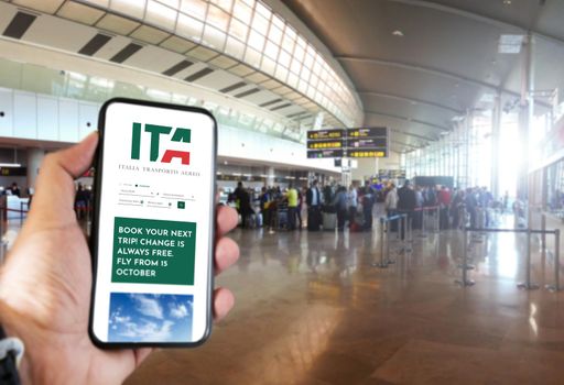 Rome, Italy, October 2021: Hand holding a smart phone with the ITA app on the screen in the airport. ITA is the new Italian flag carrier starting from 15 October 2021. Travel and vacations. Italian airliner