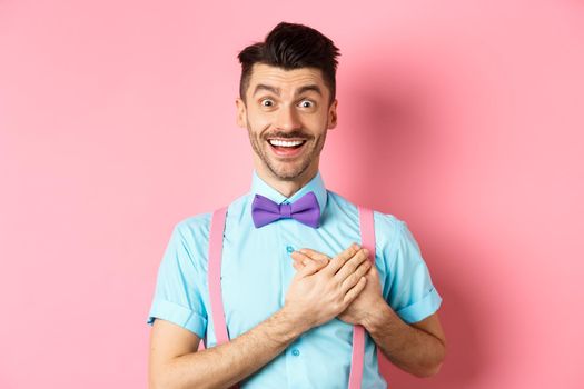 Valentines day and romance concept. Happy man in love holding hands on heart and looking with sympathy at lover, standing on romantic pink background.