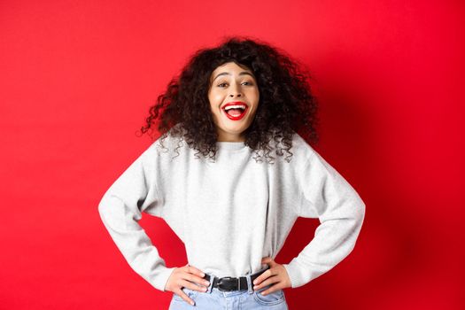 Excited positive woman laughing and smiling, feeling upbeat, looking at funny promo, standing on red background.