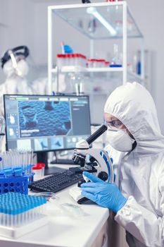 Medic and nurse dressed in ppe equipment checking evolution of coronavirus in laboratory. Scientist in protective suit sitting at workplace using modern medical technology during global epidemic.