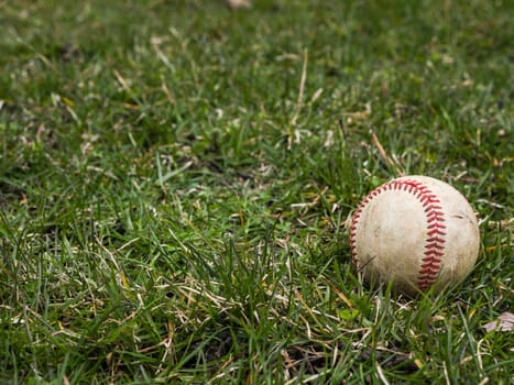 Close up sports background image of an old used weathered leather baseball ball laying in the grass field outside showing intricate detailing and red laces.