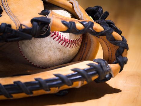 Close up sports background image of an old used weathered leather baseball with red laces inside of a baseball glove or mitt showing intricate detailing and black leather lacing.