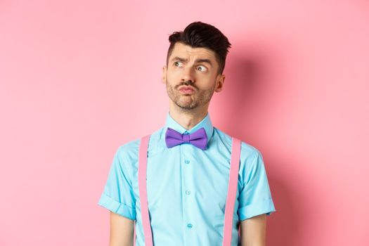 Pensive young man in romantic outfit, looking away and thinking, standing thoughtful on pink background in fancy bow-tie and shirt.