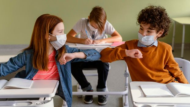 front view children with medical masks doing elbow salute class. High resolution photo