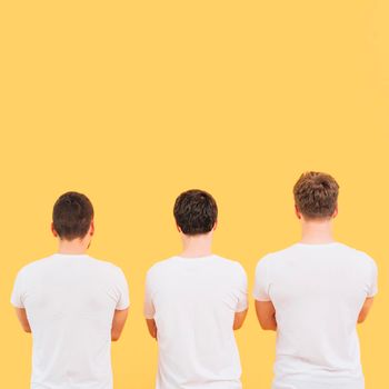 rear view men white t shirt standing against yellow background. High resolution photo