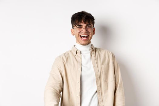 Image of happy young man laughing and looking upbeat, watching something funny, standing on white background. Authentic people concept