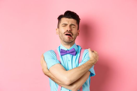 Crying guy hugging himself, feeling sad and lonely, standing unhappy on pink background. Copy space