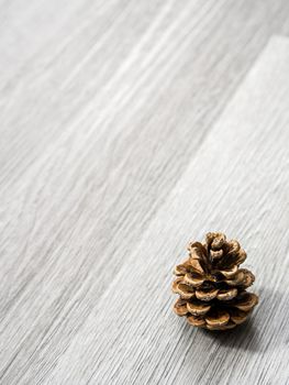 A brown pine cone laying in the corner of image and isolated on a background of gray wood grain texture flooring making a beautiful winter or Christmas holiday background.