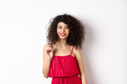 Beautiful woman with curly hair and makeup, wearing elegant dress for romantic date, standing happy on white background.