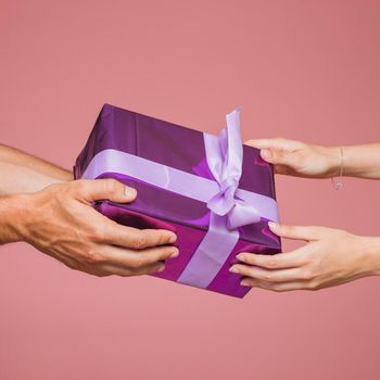two hands holding purple gift boxes against colored background. High resolution photo