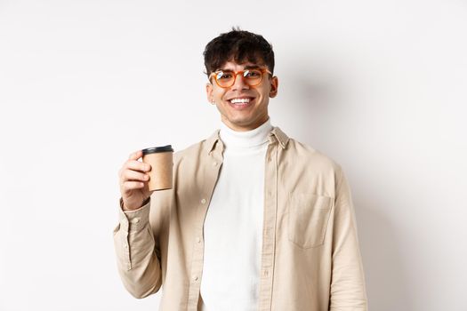 Real people. Happy young man drinking coffee from paper cup, order takeaway at favourite cafe, smiling and looking pleased at camera, white background.