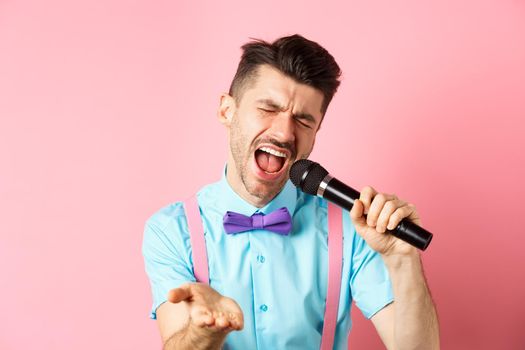 Party and festive events concept. Passionate singer holding microphone and pointing hand at you, singing about love, standing on pink background.