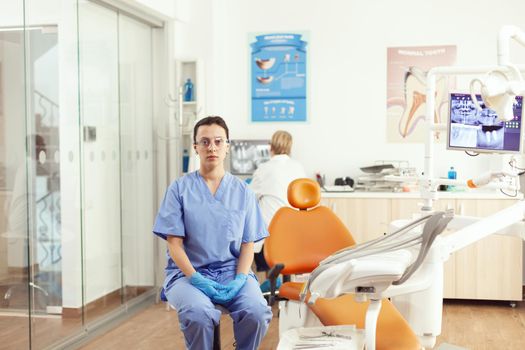 Stomatological nurse looking into camera while waiting for senior doctor to examining tooth radiography sitting in stomatology clinic office. Medical team checking dental consultation