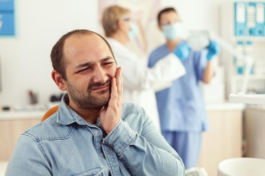 Man patient complaining about teeth pain while waiting for stomatologist doctors to check toothache. Senior orthodontic doctor and medical nurse examining x-ray working in hospital stomatology clinic