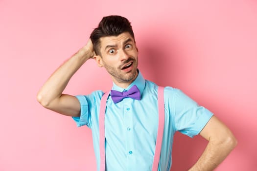 Confused funny man scratching head, staring puzzled at camera, know nothing, cant understand something, standing over pink background.