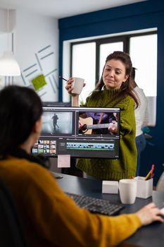 Women videographers editing video project creating content, team of bloggers sitting in modern start up office studio. Manager explaning to colleaque film montage working in post production software.