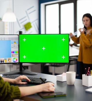 Photographer working on green mock-up screen, computer with chroma key, isolated display while sitting at desk retouching woman portrait in photo editing software. Retoucher looking at greenscreen