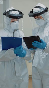 Dentist giving tablet to dental nurse before consultation appointment with patient. Stomatology doctors wearing ppe suits during pandemic while treating man for oral healthcare