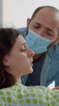 Caucasian patient in agony delivering child in hospital ward at medical clinic. Woman with contractions pushing for baby while husband and african american nurse give support and assistance