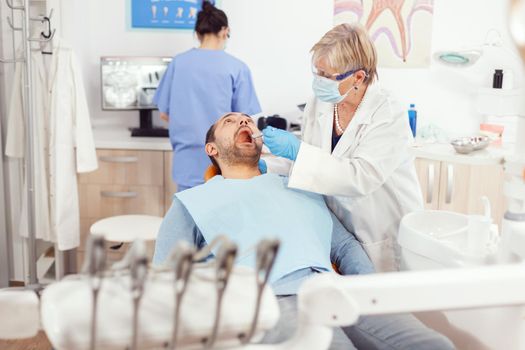 Orthodontist senior doctor doing toothache treatment on sick patient preparing surgery tools. Man lying on orthodontic chair in hospital stomatological office during medical procedure