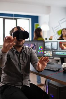 Video editor experiencing virtual reality goggles prosessing film montage in post production software sitting in creative workplace. Videographer with VR Glasses working in multimedia studio office.