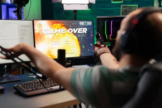 Game over for man streamer playing online space shooter game using modern headseat and joystick. Cyber performing on powerful pc talking with players on chat open during professional competition