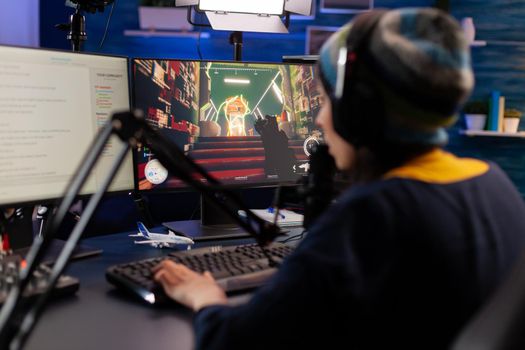 Pro gamer sitting on gaming chair at desk and talking into microphone for space shooter video games competition. Woman streaming online videogames for esport tournament in room with neon lights