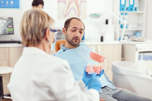 Stomatologist nurse explaining to sick man the surgery using plaster model of the Dentist dentist holding mock-up of skeleton of teeth, sample of human jaw talking. during during stomatology hospital