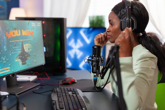 Afro american stragegy space shooter player happy after winning virtual competiton. Online streaming cyber performing during video games tournament in home with neon lights.