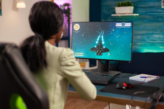 Pro african gamer playing space shooter with wireless joystick at night. Competitive cyber player woman performing videogame tournament use professional joystick.