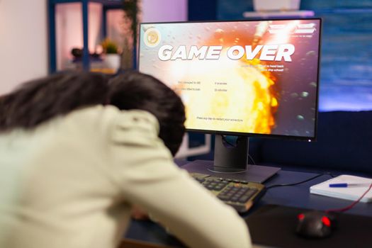 Gamer over for sad african gamer after losing championship sitting with head on the table. Angry professional gamer gaming over during an space shooter online video game.