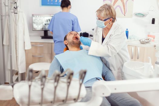 Dentistry senior woman doctor making professional teeth cleaning to sick man patient during orthodontic consultation in dental office. Hospital team examining toothache preparing tooth treatment