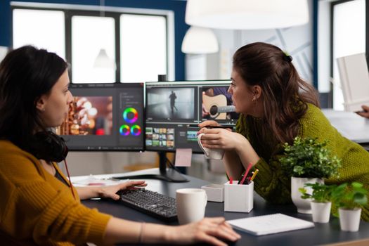 Coworkers video editors discussing in front of pc working for client footage using post production software and two monitors. Creative People processing film montage in digital multimedia company