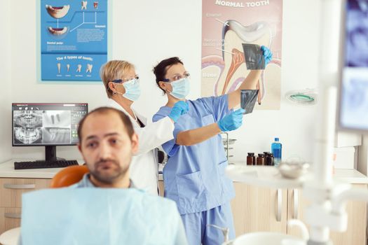 Man patient sitting on dental chair waiting for dentist doctor examining tooth radiography during stomatology appointment. Medical team checking toothache treatment working in dentistry clinic office