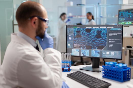 Thoughtfull doctor analyzing virus evolution on computer screen wearing protection glasses. Scientists examining vaccine evolution in medical lab using high tech, chemistry tools for scientific research.