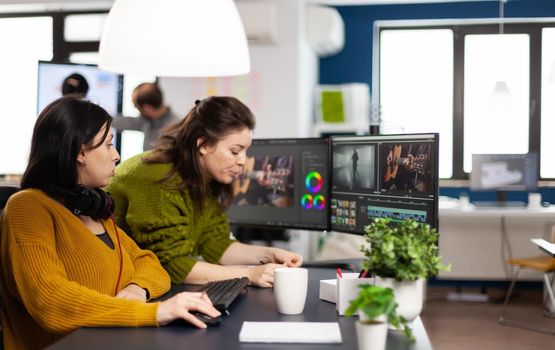 Team of women videographers working with modern post production software in digital multimedia company, looking at graphs in clipboard. Video maker employees processing film montage in creative agency