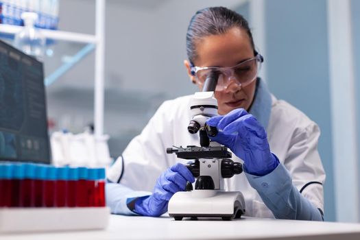 Microbiologist doctor woman analyzing vaccine results using medical microscope researching bacteriology infection diagnostics against coronavirus. Specialist doctor working in biotechnology laboratory