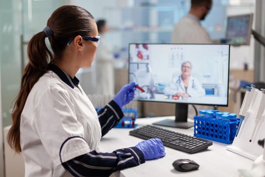 Scientist listening professional doctor on video call, during virtual meeting in medical research laboratory blood test tube. Chemist examining vaccine evolution using high tech researching treatment.