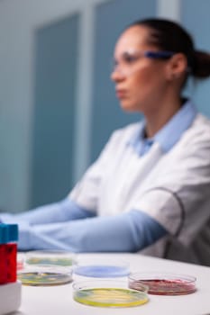 Selective focus on medical petri dish standing on table in researcher microbiology hospital laboratory. Biologist woman doctor examining microorganism sample typing expertise on computer