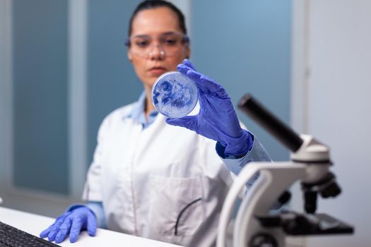 Scientist woman analyzing petri dish with microorganism bacteria in microbiology chemistry hospital laboratory. Biologist researcher working at biochemistry investigation examining microplate