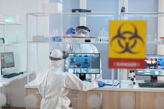 Medical staff wearing ppe suit in laboratory danger zone during pandemic. Group of doctors examining vaccine evolution using high tech for diagnosis against covid19.