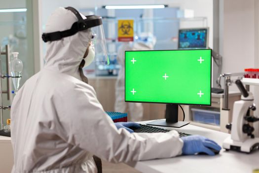 Man researcher in coverall looking at chroma key computer in modern equipped lab. Team of microbiologists doing vaccine research writing on device with chroma key, isolated display.