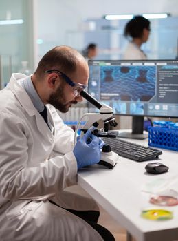 Chemist doctor looking through microscope at virus sample on patient blood to develop vaccine.. Specialists working on medicine, biotechnology research in advanced pharma lab.