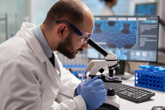 Male scientist looking under microscope at virus sample in medical development laboratory. Specialists working on medicine, biotechnology research in advanced pharma lab.