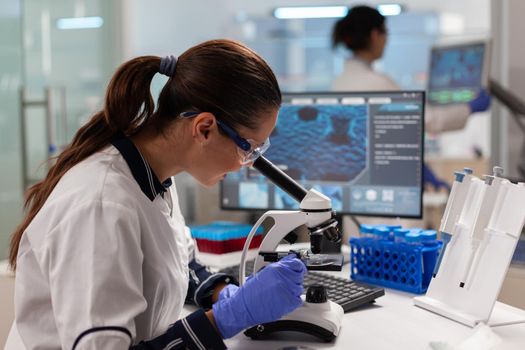 Scientist with protection glasses researching sample looking through microscope searching treatment. Medicine, biotechnology researcher in advanced pharma lab, examining virus evolution.