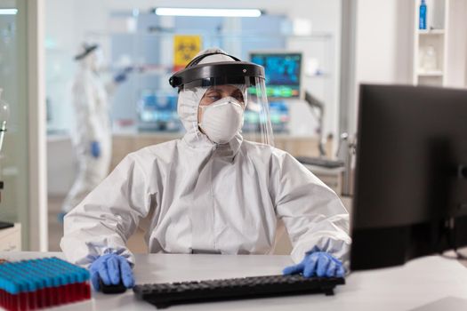 Scientist dressed in ppe suit working on computer for virus vaccine. Doctor working with various bacteria, tissue, pharmaceutical research for antibiotics against covid19.