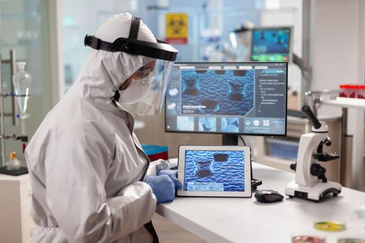 Laboratory chemist wearing ppe suit using tablet pc with virus on display. Scientist examining virus evolution using high tech technology researching vaccine development against covid19.