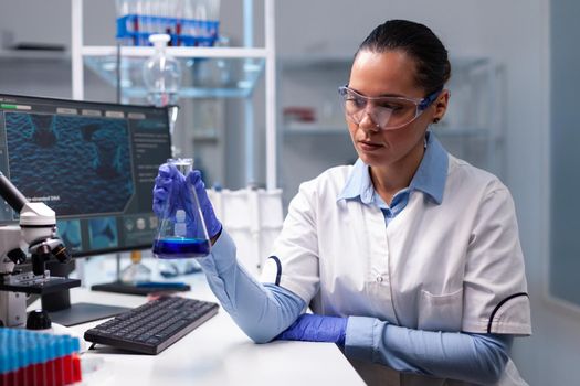 Scientist woman doctor holding glass flask analyzing liquid solution working at biochemistry experiment in microbiology hospital laboratory. Specialist researcher discovering medical diagnostic