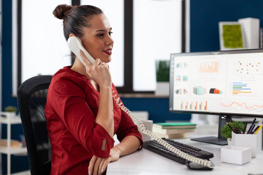 Businesswoman sitting at desk in corporate office discussing with client about important project, during phone conversation. Busy entrepreneur worker discusing contract details.